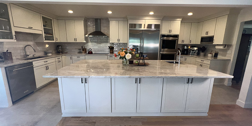 A bright kitchen with white cabinetry, a large marble island, and stainless steel appliances.