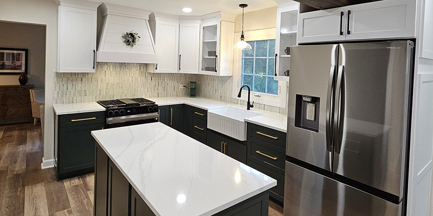 Bright kitchen with white and dark green cabinetry, featuring a farmhouse sink, stainless steel refrigerator, and a marble-like countertop.