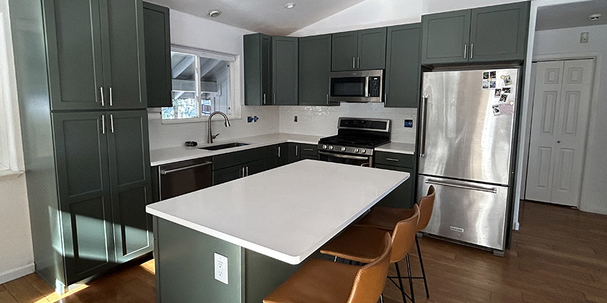 Bright kitchen with white and dark green cabinetry, featuring a farmhouse sink, stainless steel refrigerator, and a marble-like countertop.